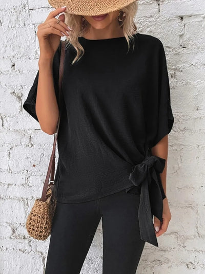 Knotted Round Neck Half Sleeve Blouse worn with black pants and a straw hat, featuring a tied detail at the waist.